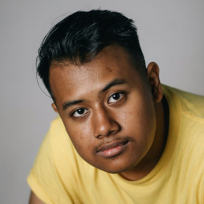 A young man in a yellow T-shirt looking into the camera.