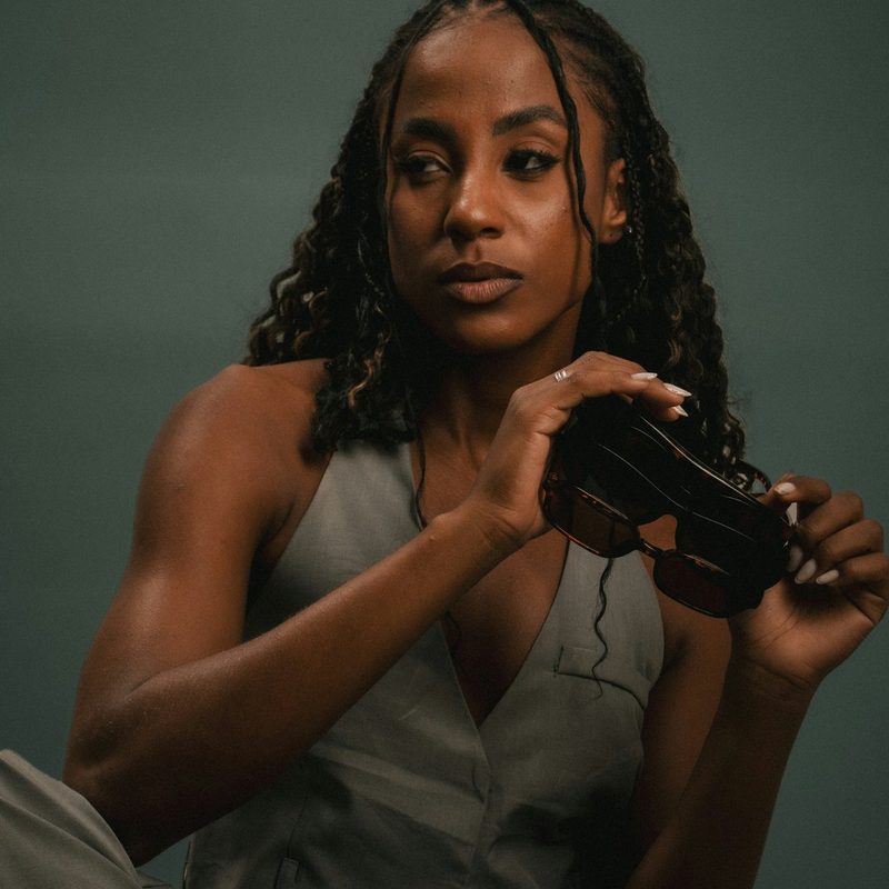 A woman with braided hair holding a film camera, looking into the lens.