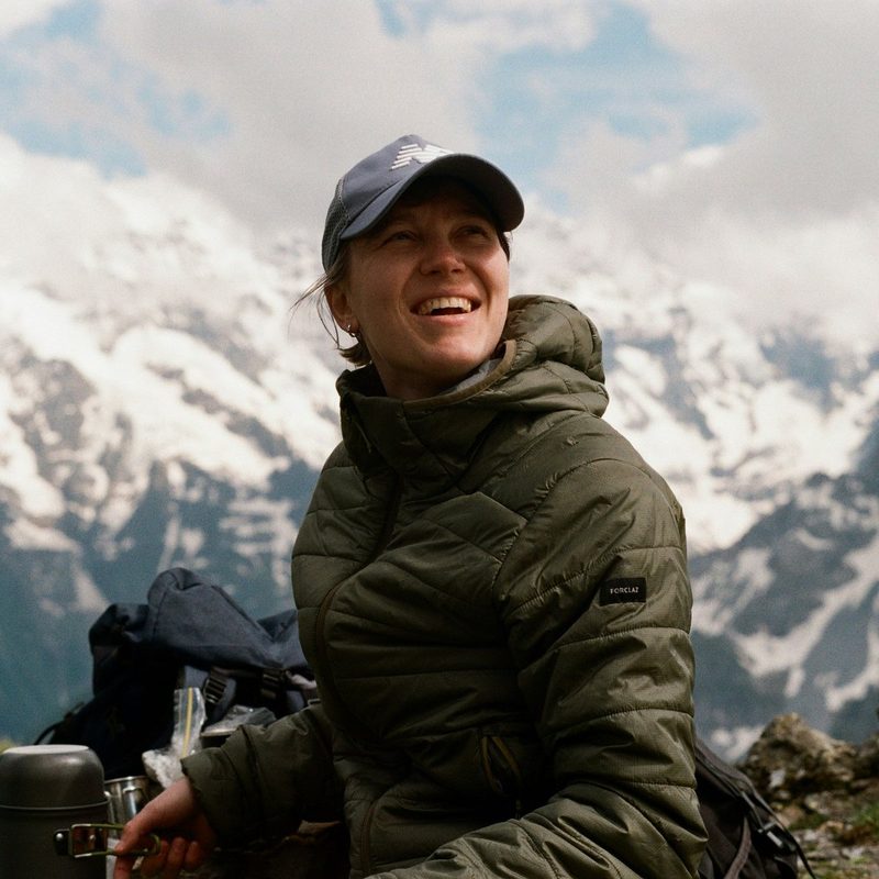 A smiling woman in a cap resting on a mountain hike.
